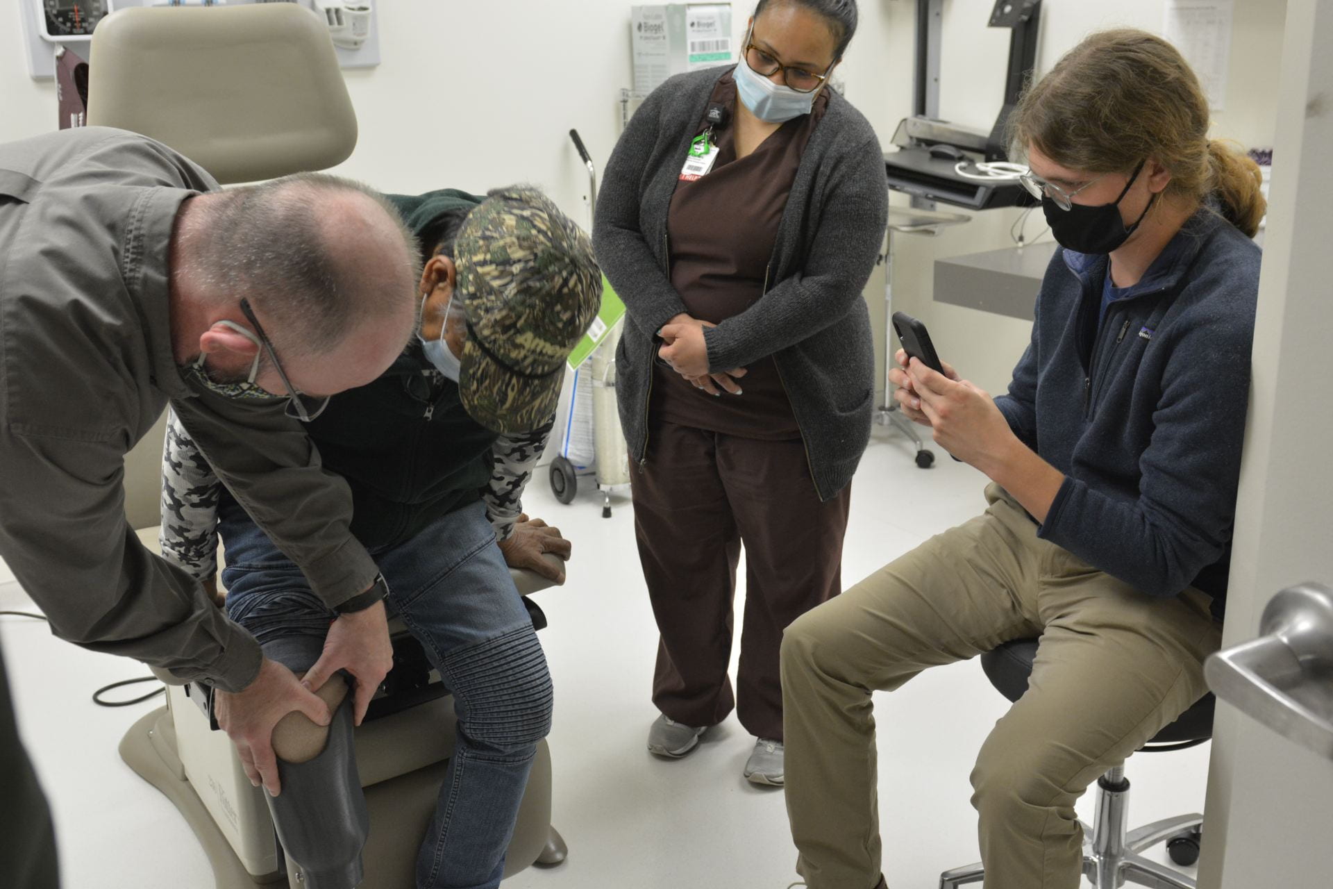 Benson Laikidrik (seated) prepares to take his first step on a new prosthetic leg as Greg Johnson from Snell Prosthetics and Orthotics (left) helps him make adjustments and student Kyle Potts (right) takes photographs